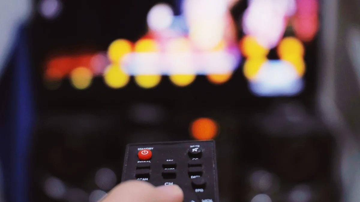 Hand med fjärrkontroll framför tv som illustrerar VPN för Viaplay och svensk streaming